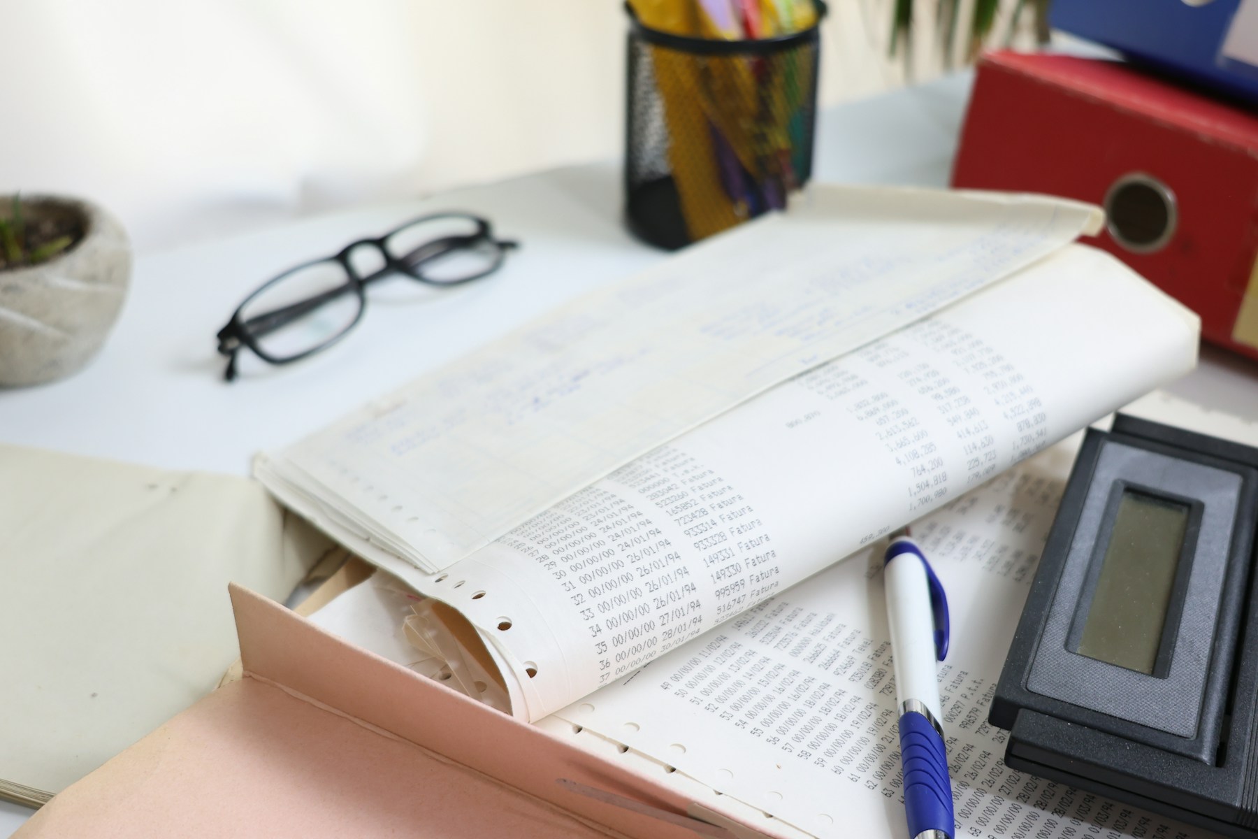 Accounting paperwork, a calculator, glasses and a pen arranged on a desk